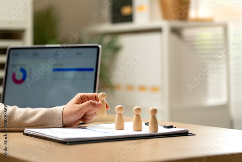 Hand holding wooden figure over clipboard with financial charts on laptop in modern office