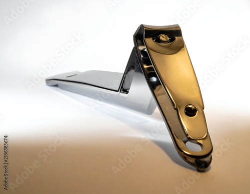 Polished gold nail clipper on white surface.