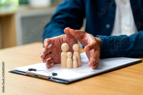 Hands gently cradling wooden family figures over financial documents on wooden desk