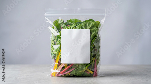 Fresh Organic Green Chard in Transparent Plastic Bag with Blank White Mockup Label for Branding and Packaging Design on Studio Background