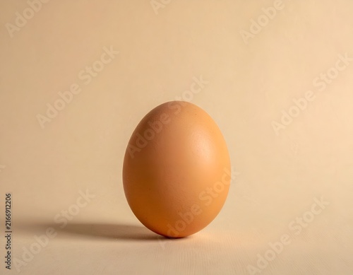 Whole brown egg standing on beige background.