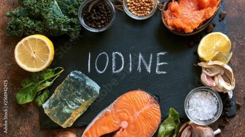 Various natural food sources rich in iodine with fresh salmon, seaweed, lemon, garlic, kale, spinach and spices on dark rustic background for healthy diet and nutrition