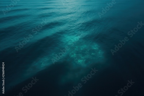 Calm ocean surface viewed from above, with gentle ripples and waves in varying shades of blue and turquoise, sunlight revealing depth and serene natural beauty of water.