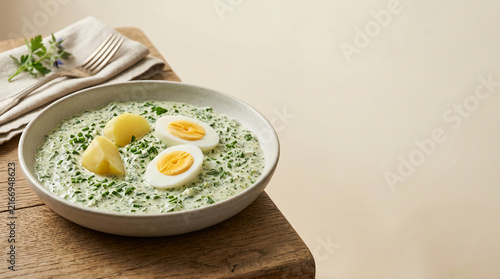 Comforting bowl of traditional creamy green herb sauce with tender boiled potatoes and halved hard-boiled eggs, presented on a rustic wooden table