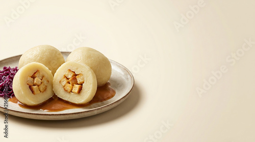 Homemade Potato Dumplings Stuffed with Crispy Croutons Served with Red Cabbage and Savory Gravy on a Ceramic Plate