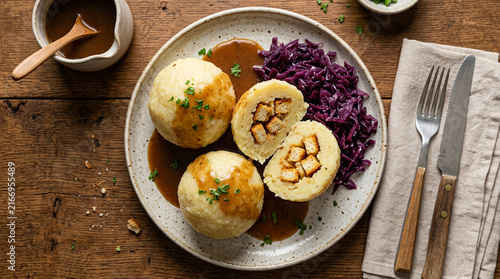 Hearty German Dumplings with Crouton Filling Served with Red Cabbage and Savory Brown Gravy on a Rustic Wooden Table