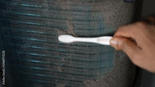 Hand cleaning dusty metal fins with a toothbrush, Close-up of a hand using a toothbrush to clean dust from metal cooling fins