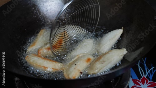 Dumplings frying in hot oil inside a wok with a metal spatula, showing home cooking, sizzling food preparation and golden browning.