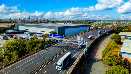 Fotografía Freight trucks moving along elevated motorway near large distribution warehouse