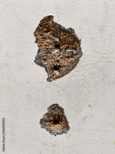 Fotografie Damaged Wall Texture: A close-up shot reveals the weathered texture of a wall with a large hole and smaller divots, showcasing its aged and worn appearance