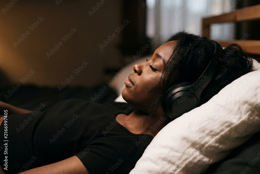 Fototapeta premium Woman resting on bed with headphones in peaceful home setting