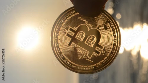 Bitcoin coin. Person holding Bitcoin coin in hand on background sea, blue sky and shining sun at dawn and sunset. Concept cryptocurrency money cryptography cryptocurrencies bitcoins. Vertical