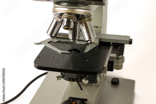 Detailed view of the optical and mechanical components of an old scientific microscope, including objective lenses, specimen holder, graduated stage and focusing mechanisms.