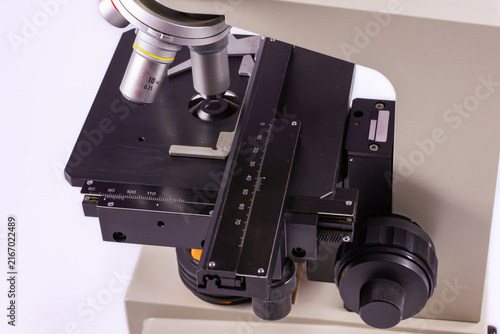 Detailed view of a scientific microscope featuring a calibrated mechanical stage, adjustment knobs and specimen platform designed for precise microscopic examination.