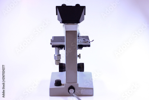 Classic scientific microscope photographed from the rear, showing binocular eyepieces, precision adjustment knobs, specimen stage and sturdy metal frame for laboratory research.