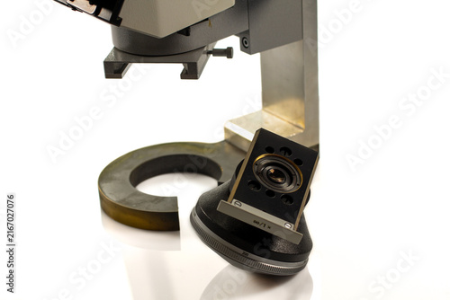 Close-up of a vintage microscope condenser assembly with optical lens, rotating adjustment ring and sturdy metal support, photographed on a clean white background.