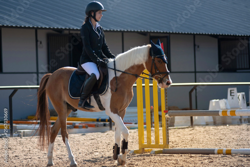 teenage girl in riding attire waits on her horse, anticipating being called to participate in the show jumping competition on the track.