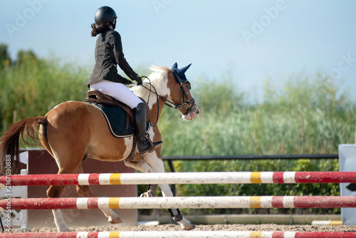 Teenage equestrian girl in her competition attire is participating in show jumping on the course.