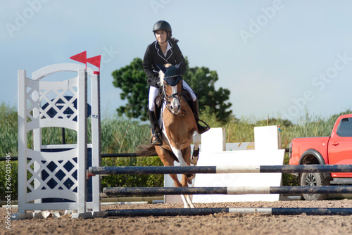 Teenage equestrian girl in her competition attire is participating in show jumping on the course.