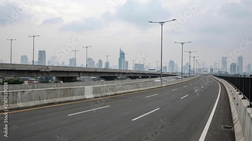 Timelapse of fast moving cars on a highway overpass with city skyline in the background during a cloudy day