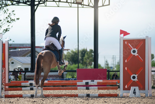 Teenage equestrian girl in her competition attire is participating in show jumping on the course.