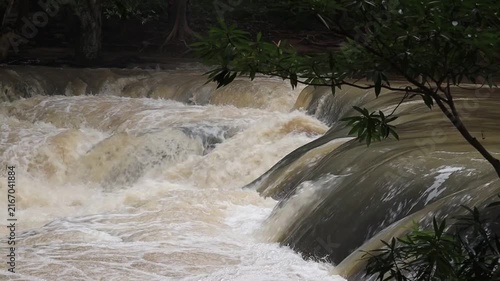 Turbulent Cascade: A powerful waterfall surges over rock formations, creating a dramatic display of nature's raw energy and force, surrounded by lush foliage.