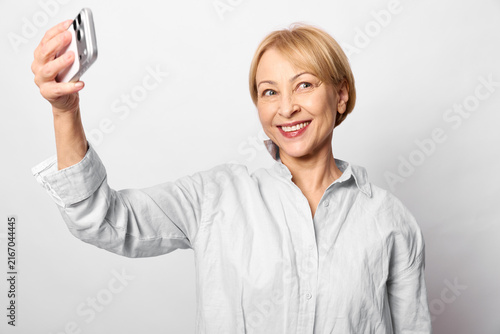 Fotografie Senior woman takes selfie with smartphone, smiling portrait in clean white backg