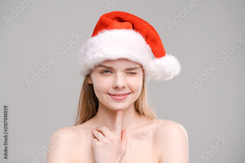 Принти на полотні Playful Winking Woman in a Santa Hat on a Grey Background