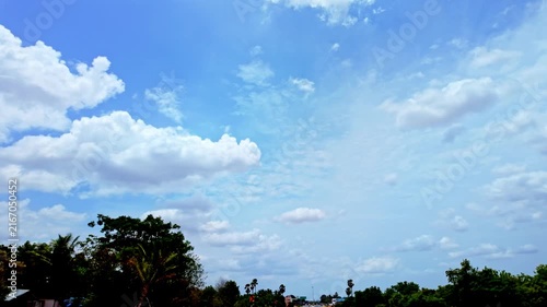 Fluffy Cumulus Clouds Across Blue Sky Over Treeline