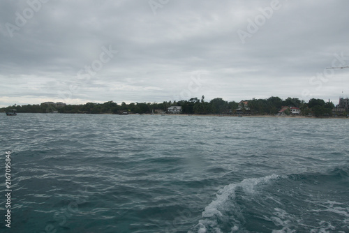 Cuadro en lienzo A distant tree-covered island forms a narrow horizon beyond gently rippled tropical water