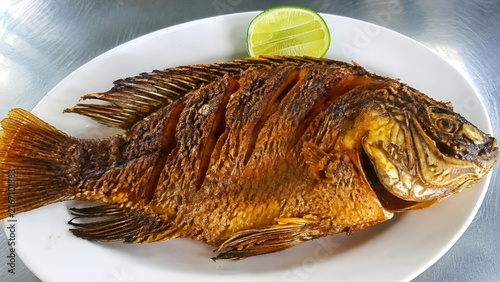 Crispy Whole Fried Tilapia Served with Fresh Lime Wedge on White Oval Plate