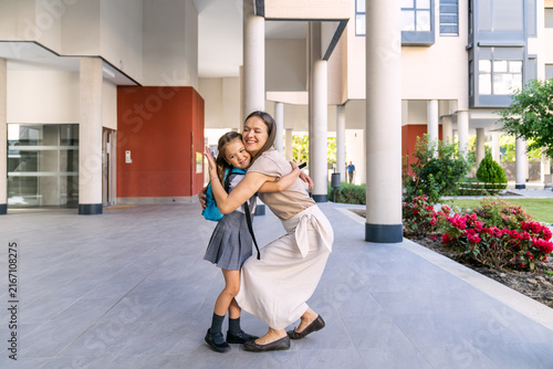 Happy mother hugging her excited daughter wearing school uniform and backpack, celebrating back to school moment