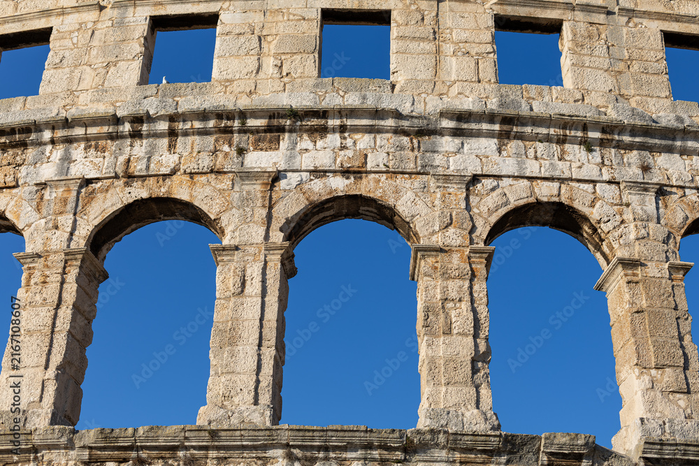 Obraz premium Ancient Arches of Pula Arena Roman Amphitheater in Croatia. Close view of ancient stone arches and weathered masonry of Pula Arena in Croatia against a clear blue sky.