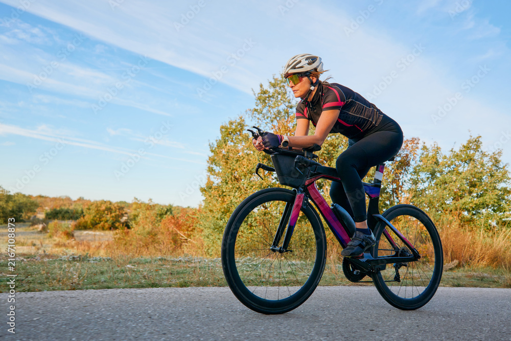 Fototapeta premium Female Cyclist Riding Aerodynamic Road Bike on Country Road During Sunny Outdoor Training Session