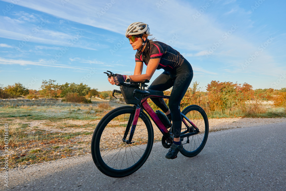 Fototapeta premium Female Cyclist Training on Road Bike at Sunrise With Aerodynamic Helmet and Sunglasses