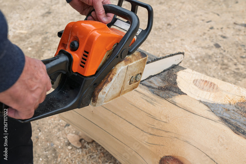 professional lumberjack saws logs, holding a chainsaw in his hand, to build wooden house.