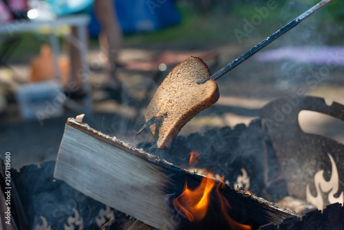 Slices of bread toasted over an open campfire on a metal skewer, creating a rustic outdoor cooking scene. High quality photo