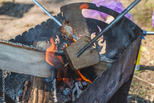 Slices of bread toasted over an open campfire on a metal skewer, creating a rustic outdoor cooking scene. High quality photo