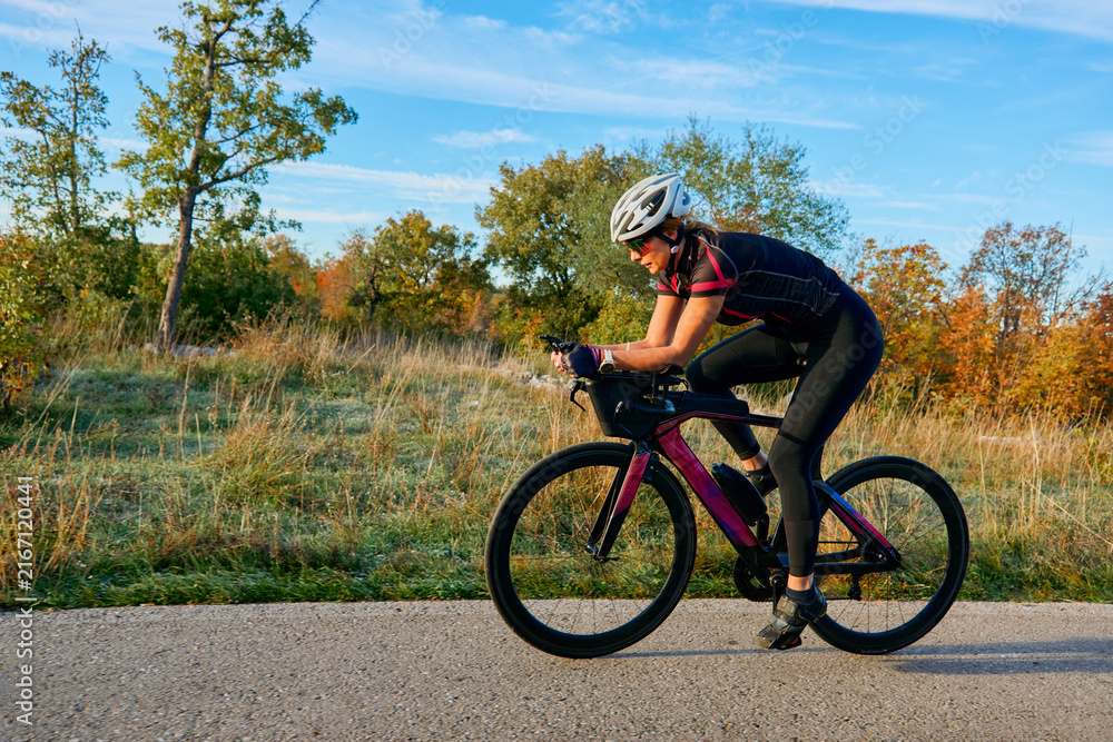Fototapeta premium Female Cyclist Training on Road Bike in Autumn Countryside for Fitness and Triathlon Preparation
