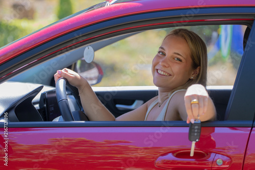 Young woman smiling and holding car keys while sitting in the driver's seat of her new car, celebrating her first vehicle purchase
