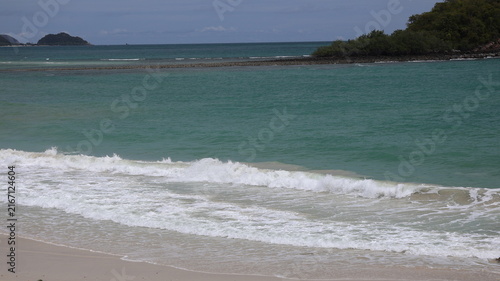 Foto The image depicts a calm beach scene with gentle waves lapping against the sandy