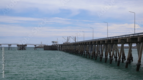 Bild auf Leinwand The image depicts a long pier extending over calm water, supported by numerous w