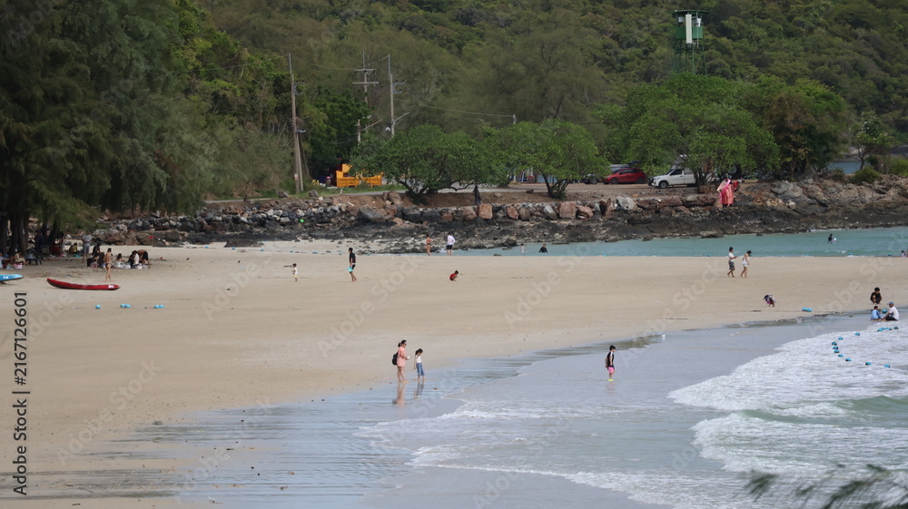 Obraz premium The image depicts a sandy beach with several people enjoying the shoreline. Some individuals are walking along the water's edge, while others appear to be playing or relaxing near the surf