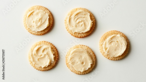 Crunchy biscuits topped with spreadable cheese on plain white backdrop