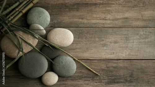 Smooth spa stones and bamboo stalks arranged on a rustic wood surface, seen from above.