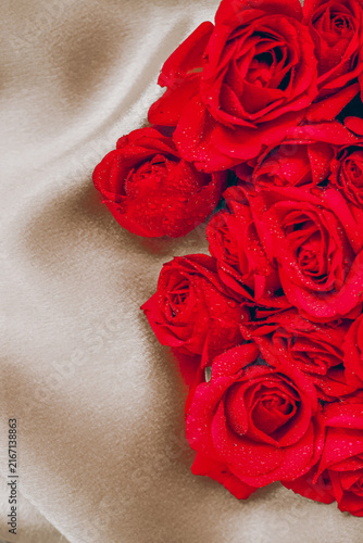 Bild auf Leinwand Red roses on a soft fabric background with droplets of water in an indoor settin