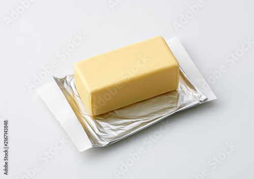 A single stick of butter in its silver foil wrapper on a white background.