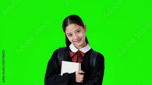 Happy schoolgirl smiling and raising her hand on green screen background, young student ready to answer a question for education, learning and classroom concepts