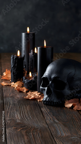 Dark Halloween setting with black candles and skull on wooden table