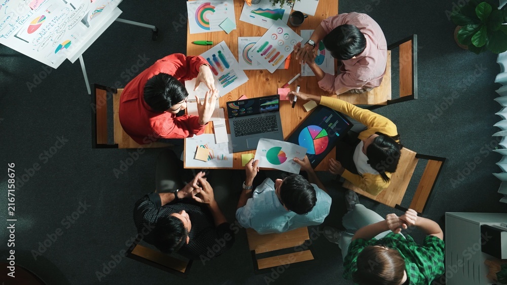 Fototapeta premium Top view of business team working together while talking about financial chart. Close up of skilled marketing team sharing idea and looking at stock market statistic chart at boardroom. Convocation.